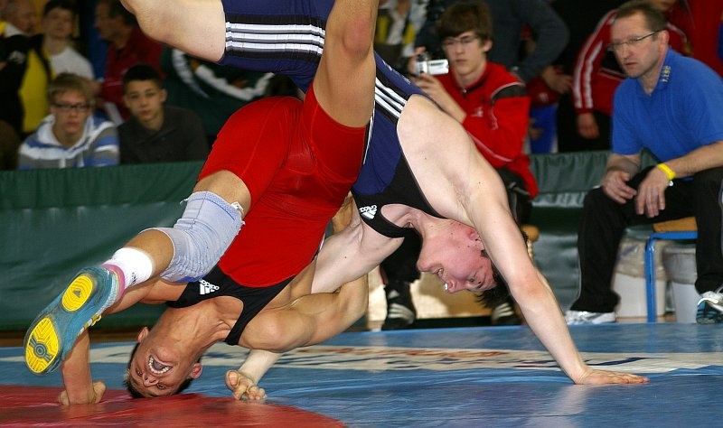 DM_OlbernhauSonntag002.jpg - ... so dass er auch am Sonntag starten durfte. Hier sieht man ihn beim Kampf um Platz drei. Diesmal trägt er rot und kämpft gegen Marcel Strubel aus Württemberg.Die gezeigte Technik wird ihm einen Punkt bringen, da er seinen Gegner aus dem Innenbereich in den blauen Außenbereich befördert. Dies bringt eine Wertung für den angreifenden Ringer. Mit der Einführung dieser Regel hat man das "Weglaufen", das vorher bei Führungen sehr verbreitet war, sehr gut unterbunden.Diesen Kampf gewann Wickel ziemlich deutlich, in der ersten Runde hatte er sogar sechs Punkte Vorsprung, was sofort zu einem (Runden-)Sieg durch "Technische Überlegenheit" führt. Somit erhielt er die Bronzemedaille.