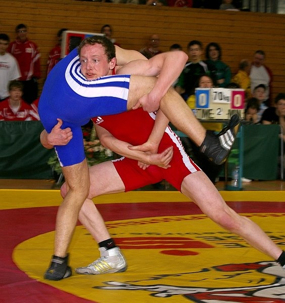 DM_OlbernhauSonntagFinalkaempfe048.jpg - Manchmal reichen aber auch Nuancen nicht aus. Nachdem Thorsten Preiß (blau, Bayern) Runde eins 0:2 gewonnen hatte, konnten beide Ringer in den folgenden zwei Minuten keine Wertung erzielen. Das bedeutet beim Ringen, dass das Glück entscheiden muss.Der Kampfrichter wirft eine Münze die entscheidet, wer zum "Zwiegriff" an das Bein des Gegners fassen darf. Dann wird angepfiffen und die nächste Wertung bringt den Sieger.Das Los entschied für Florian Fischer (rot, Hessen). Sofort mit dem Anpfiff nutzte er diesen Vorteil um die Runde zu gewinnen. In der dritten konnte er sich auch durchsetzen und wurde somit Deutscher Meister in der Gewichtsklasse 69 kg.